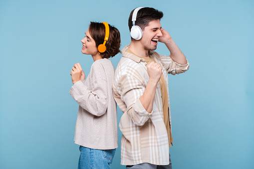 Young fun couple two friends family man woman wear casual clothes headphones listening music, singing song together isolated on blue color background studio