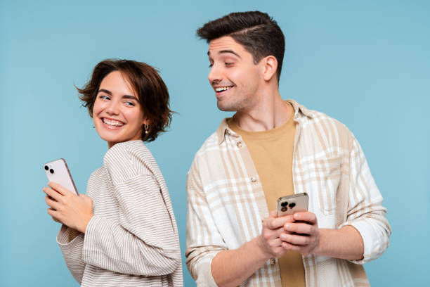 istock Curious man looking at smartphone of his girlfriend isolated on blue background 2015097656