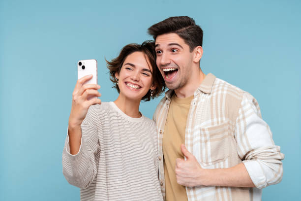 istock Young smiling friends hugging holding mobile phone making selfie over blue wall background 2015097664