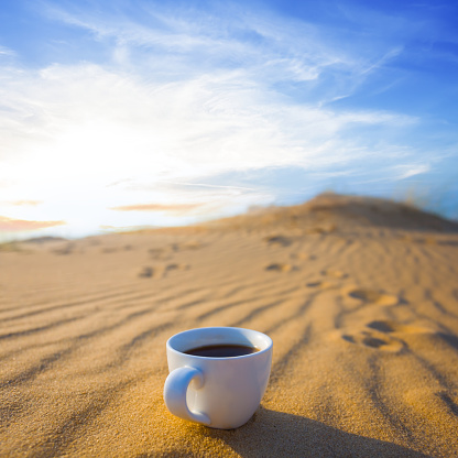 closeup white coffee cup on wavy sand at the sunset