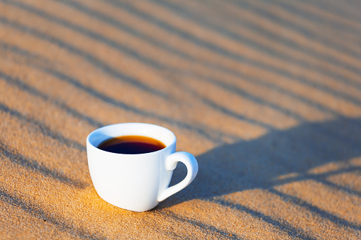 closeup white coffee cup on wavy sand