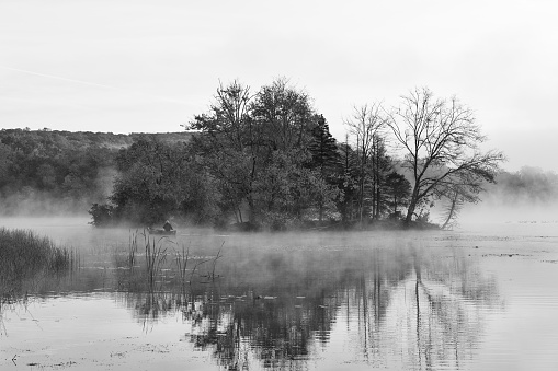 Elverson, USA - October 18, 2020. Morning mist over Hopewell Lake with a man on boat, French Creek State Park, Elverson, Pennsylvania, USA