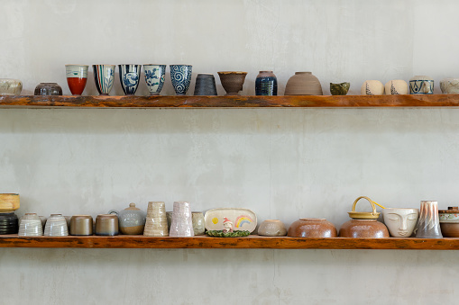 Many designed ceramic and pottery, bowl, mug for hot drinks decorated on the wood shelves and bare concrete wall, rustic and vintage