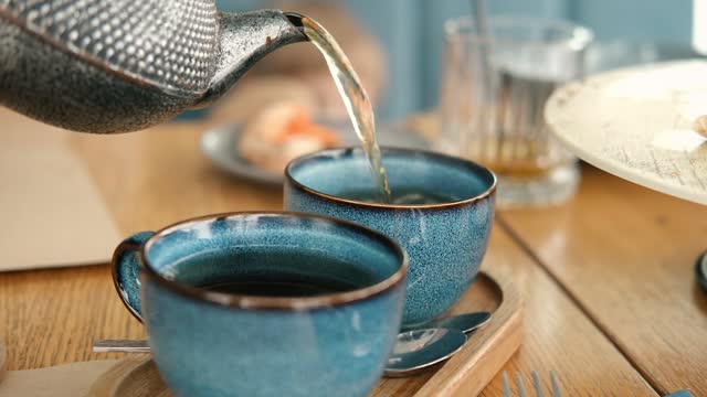 Brewing and Serving Tea. Teapot Pouring Green Tea in Blue Ceramic Cup on Wooden Cafe Table. Two Pottery Handmade Mugs Early in the Morning. Trendy Authentic Porcelain Set. Breakfast Concept. Tea Time.