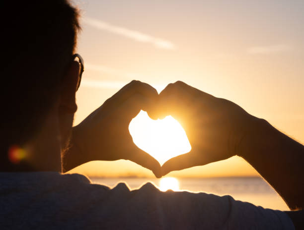 istock man hands forming a heart shape with sunset silhouette 2015221527
