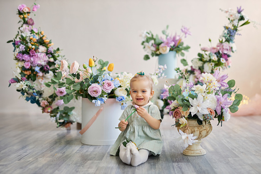 Charming Little cute girl in a bright spring studio, many flowers, bouquets
