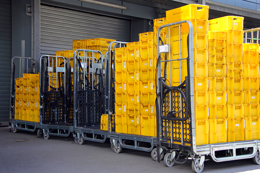 Fuerth, Germany - April 6, 2015: many empty yellow transport boxes of DHL and Deutsche Post in Germany at daylight. Stacked transport boxes in trolleys at a distributor center.