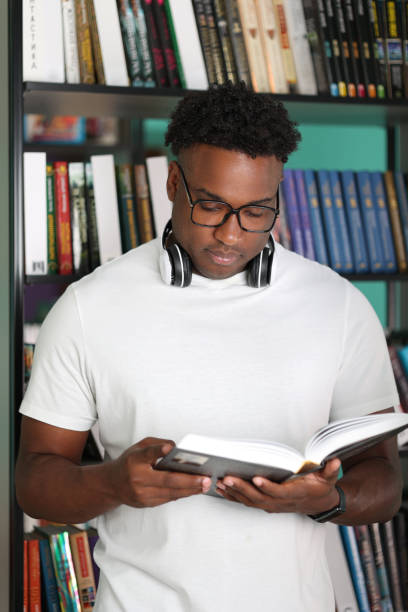 istock Young serious african student reading and studying among bookshelves in library 2015273999