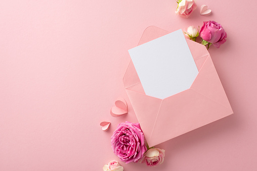 Happy 8th of March frame. A top view capture of a revealing envelope, emotive card, paper heart cutouts, and radiant rose petals on a soft pink background, reserving space for text or marketing