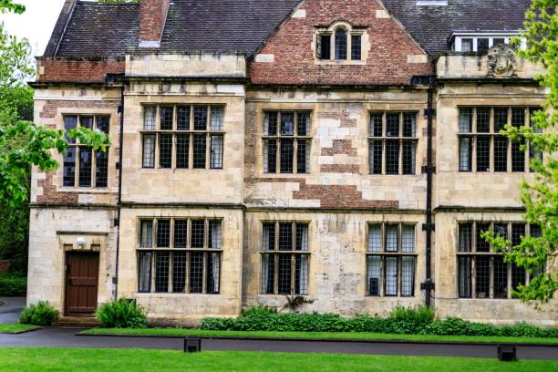 York, UK. June 2, 2024.  Two ancient buildings, a part of Kings Manor in York, stand in the sunshine surrounded by trees. A sky with cloud is above.