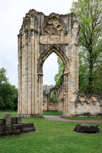 York, UK. March 14, 2025.  The ancient ruins of a Norman Abbey.  A tall archway stands in the centre and a line of stonework lies on the ground leading up to the arch. A cloudy sky is above.