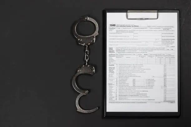 Photo of Handcuffs over Tax forms, concepts: Tax fraud or Slave to the Taxes