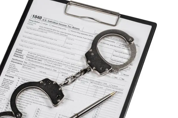 Photo of Handcuffs over Tax forms, concepts: Tax fraud or Slave to the Taxes