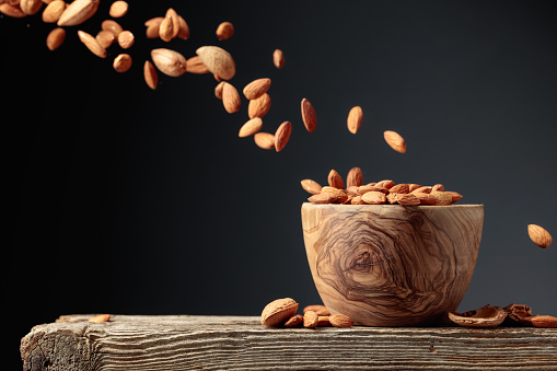 Almond is poured into a wooden bowl. Frontal view with copy space.