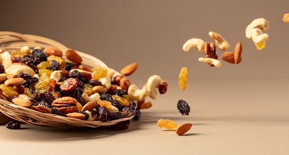 Flying dried fruits and nuts. The mix of dried nuts and raisins on a beige background. Copy space.