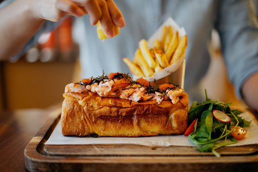 Close up shot of an Asian Woman squeezing lemon onto lobster roll in before eating