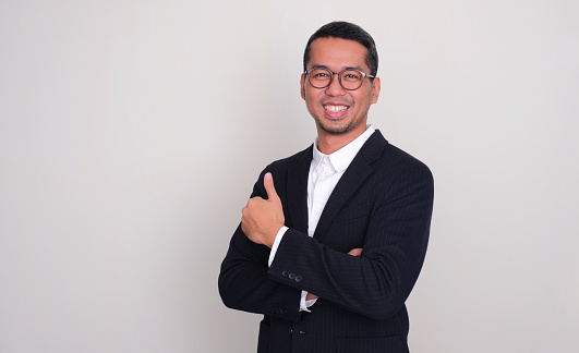 Asian businessman smiling confident at the camera and giving thumb up