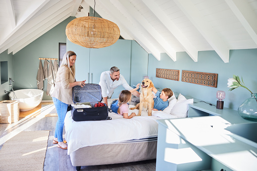 Smiling parents unpacking suitcases on a bed next to their two children and the family dog during a vacation together