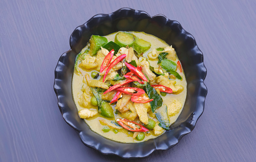 Chicken green curry in black ceramic bowl on wooden table top, Traditional Thai food style, Flat lay with copy space