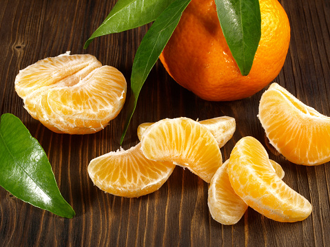 Seedless Mandarin Fruit Segments with Leaves on wooden Background