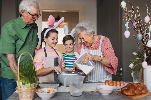 Grandparents with grandchildren preparing traditional easter meals, baking cakes and sweets. Passing down family recipes, custom and stories. Concept of family easter holidays.