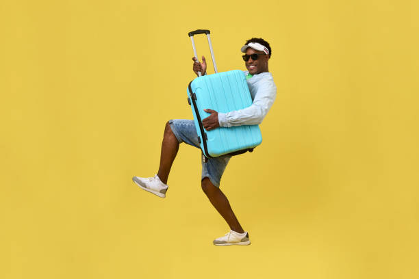istock Funny African guy holding big blue suitcase by handle in hand stepping forward 2015390383