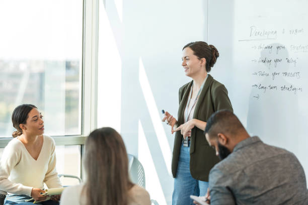 istock Mid adult female supervisor smiles while talking to her peers about goal setting techniques 2015415010