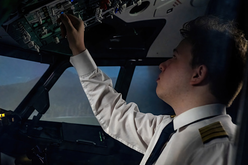 Captain makes precise adjustments to dashboard in cockpit. Young pilot carefully checks and rechecks configurations during flight