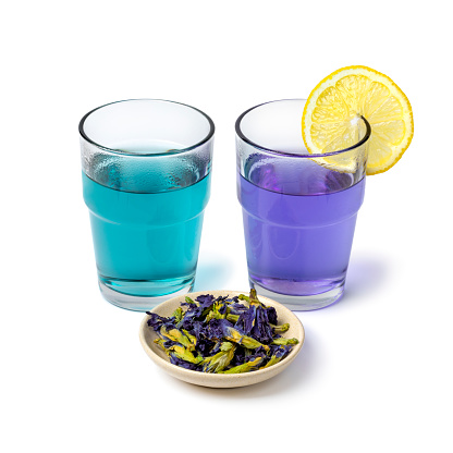 Glasses with blue and purple Butterfly pea flower tea with lemon and dried butterfly pea tea flowers close up isolated on white background