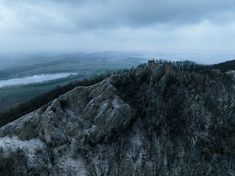 Aerial view of old ruins of fortress in the middle of winter forest. Drone view of snowy landscape with broken stone walls. Castle ruins.