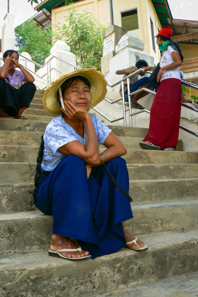 Bagan, Myanmar - July 16, 2008: Burmese woman wearing straw hat for sun protection sitting on stairs looking into the camera, Myanmar, Burma, Asia