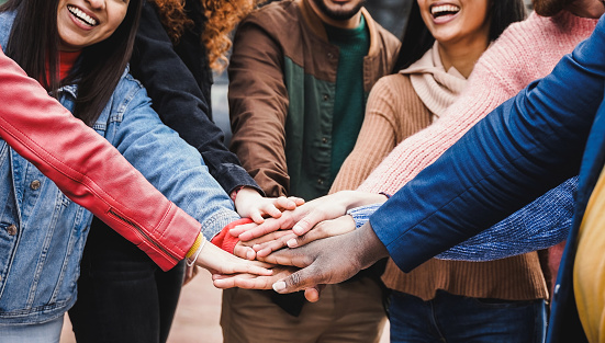 Happy group of people stacking hands together. Friends team celebrating outside. Diversity and unity concept