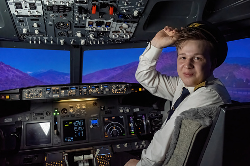 Man pilot in hat sets autopilot on airplane during flight. Captain allows technology to assume control of aircraft among mountains