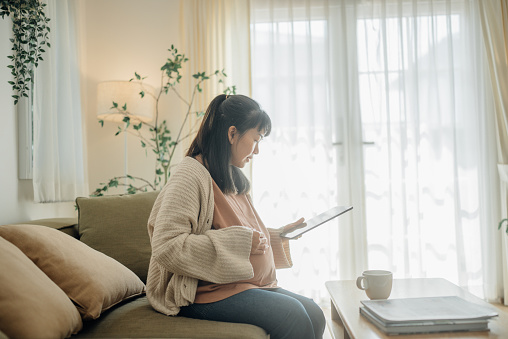 Side view of cheerful pregnant woman looking ultrasound images on a digital tablet at home.