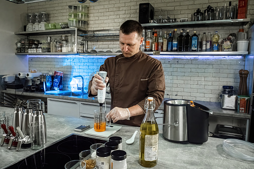 Man chef uses immersion blender mixing ingredients for spicy sauce. Professional cook in uniform uses modern kitchen devices for cooking