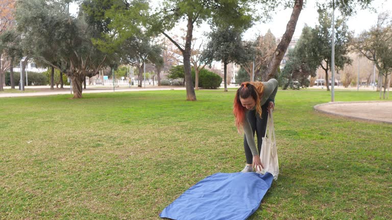 A woman spreads a blue blanket on the grass in a park