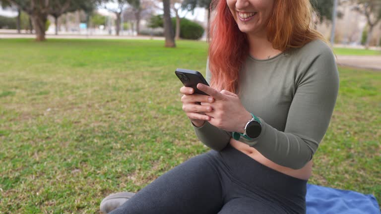 A woman sitting on grass, focused on her smartphone