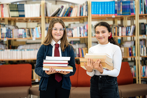 Two female junior high school students holding books in the school library