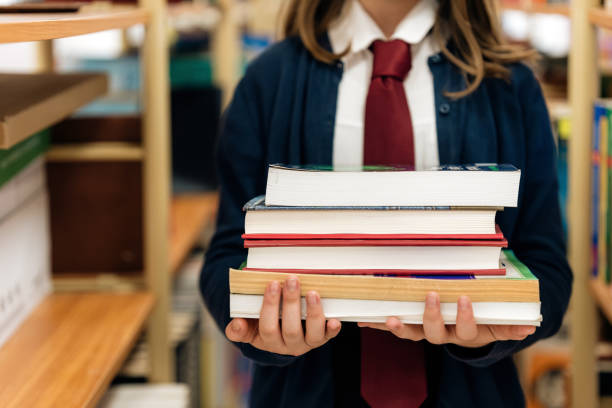 Close-up of female junior high school student holding a stack of books in the school library