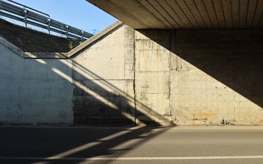 Grunge concrete wall of an underpass divided in two by the sunlight. Two lane road in front, guard rail of another street in the upper side. Background for copy space