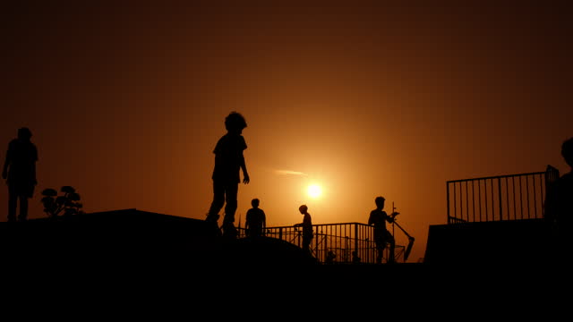 Silhouettes on skateboard ramp in evening.