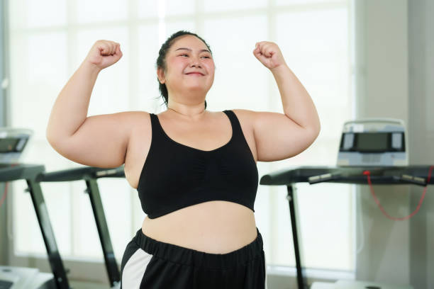 istock Plus-size Asian woman exercise in gym, Exuberant  flexing muscles, showing strength and joy, treadmill machines in behind, flexing biceps, displaying strength and happiness in fitness setting 2015561856