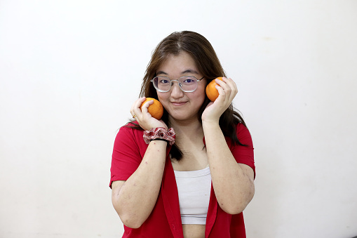 Portrait shot of an Asian teenage girl holding mandarin oranges and smiling at the camera