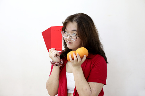 Portrait shot of an Asian teenage girl holding mandarin oranges and red envelopes (hong bao) and smiling