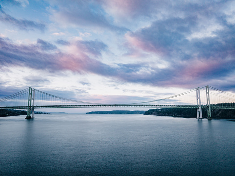A few of the sunrise coloring the clouds pink and purple on a cold winter morning looking toward the Tacoma Narrows suspension bridge, spanning the Puget Sound between Gig Harbor and Tacoma, Washington.  USA.