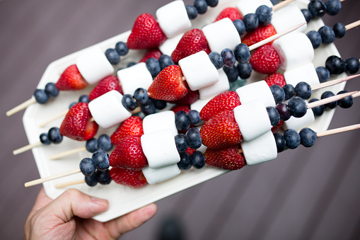 A person holds a tray of red white and blue fruit skewers, a fun and festive snack for the 4th of July  Independence Day holiday in the United States of America.