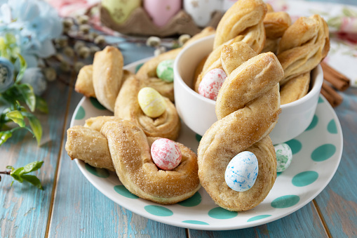 Easter rabbit-shaped buns puff pastry with  cinnamon on a wooden blue tabletop. Easter bake idea, holiday food 2024.