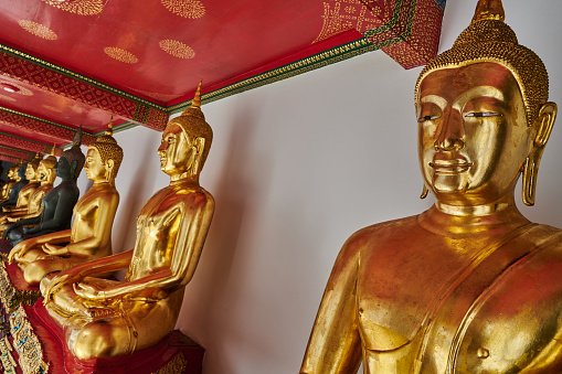 A single candle burns among the golden statues of the deity. An oriental god with a staff and beads looks into the distance. It is covered with a fan of leaves. The Temple of Big Buddha. Yellow candle