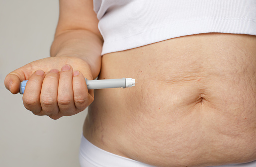 Female belly and hand closeup with Semaglutide Injection pen or insulin cartridge pen. Medical equipment for diabetes patient. Diabetes and weight loss concept.