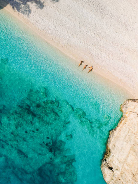 People relaxing and aunbathing on beach with clear sea water Three women enjoying sunbathing at morning on the beach with in crystal clear water with beautiful color. Famous Fteri beach, island of Kefalonia, Greece kefalonia stock pictures, royalty-free photos & images